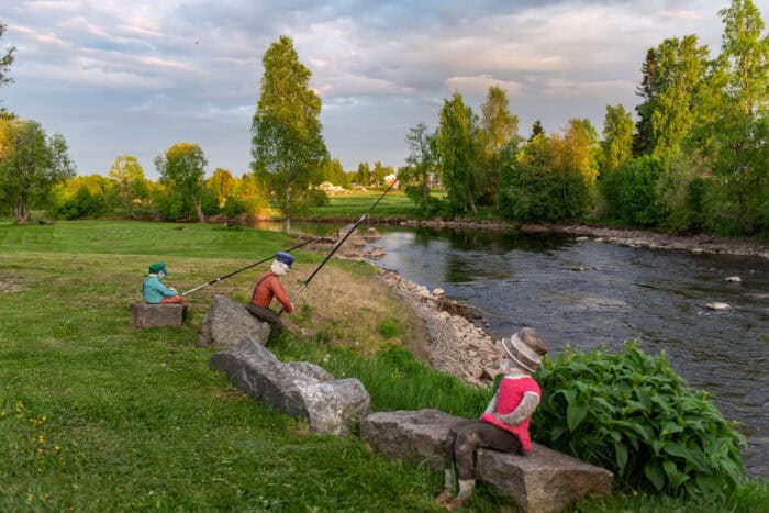 Virtaava joki, joen rannalla kolme patsasta, vihreä luonto.